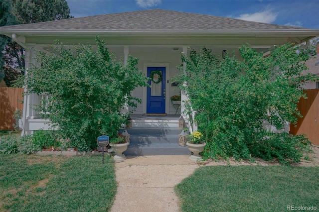 doorway to property featuring a shingled roof, fence, and a lawn