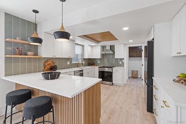 kitchen featuring stainless steel appliances, a raised ceiling, decorative backsplash, a peninsula, and wall chimney exhaust hood