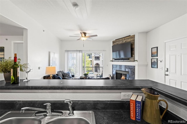 kitchen with open floor plan, a ceiling fan, a sink, a fireplace, and dark countertops