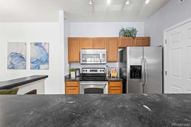 4451 S Ammons St Unit 4-203, Littleton, CO 80123 - kitchen with stainless steel appliances, dark stone counters, rail lighting, and brown cabinetry