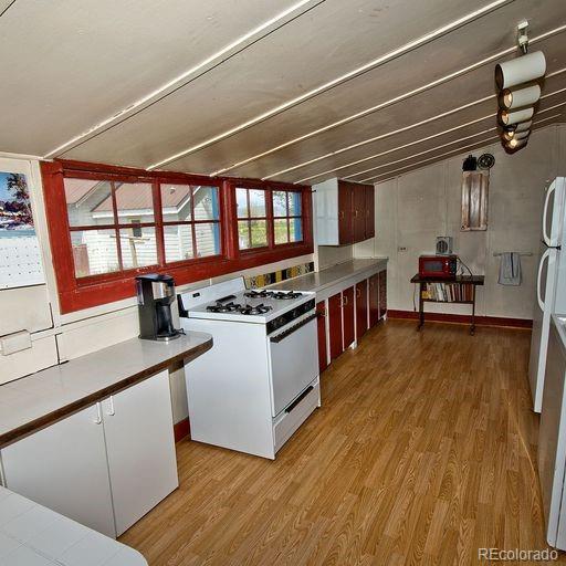 kitchen featuring lofted ceiling, light hardwood / wood-style floors, white cabinetry, and white appliances