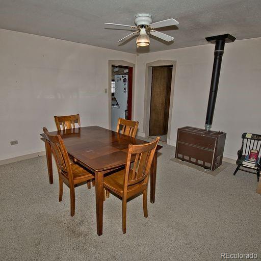 carpeted dining area featuring ceiling fan and a wood stove