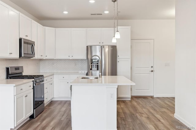 kitchen with appliances with stainless steel finishes, decorative light fixtures, white cabinetry, backsplash, and a center island with sink