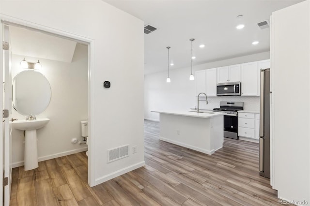 kitchen featuring appliances with stainless steel finishes, tasteful backsplash, white cabinetry, pendant lighting, and a center island with sink