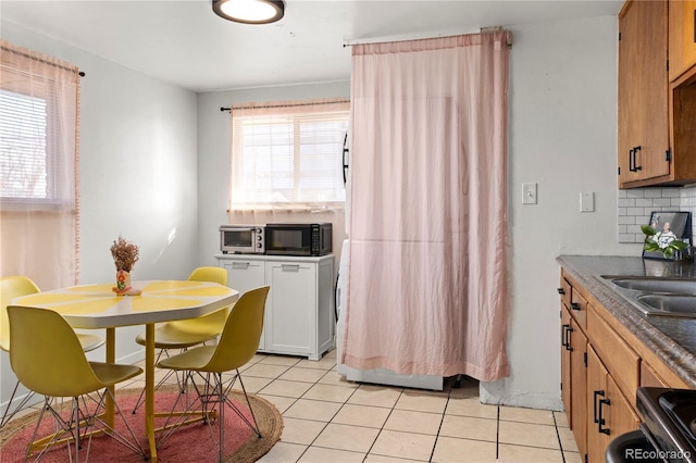 kitchen featuring black microwave, light tile patterned floors, backsplash, and a wealth of natural light