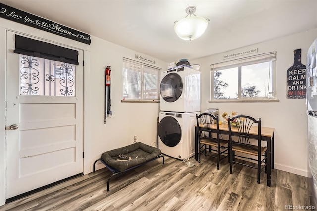 laundry area with baseboards, laundry area, wood finished floors, and stacked washer / drying machine