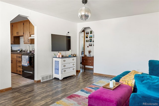 living area featuring arched walkways, visible vents, baseboards, and wood finished floors