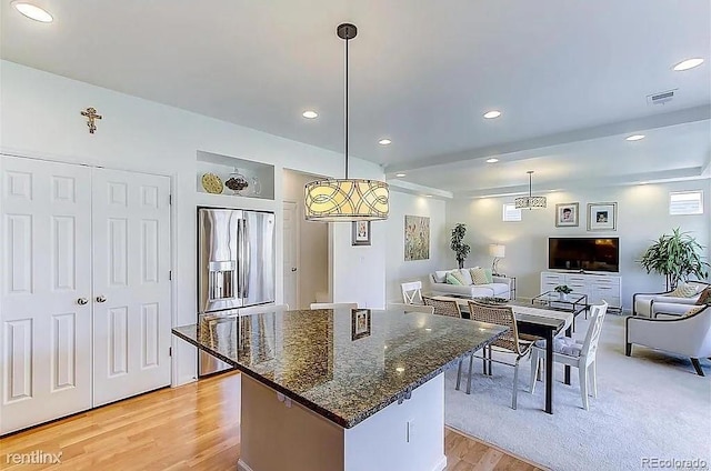 kitchen with stainless steel refrigerator with ice dispenser, a center island, light hardwood / wood-style flooring, hanging light fixtures, and dark stone countertops