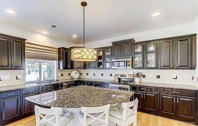 kitchen with stainless steel appliances, decorative light fixtures, a center island, and dark stone counters