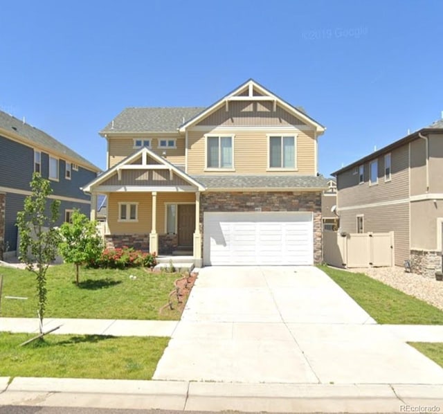 craftsman-style home featuring stone siding, driveway, a front lawn, and fence