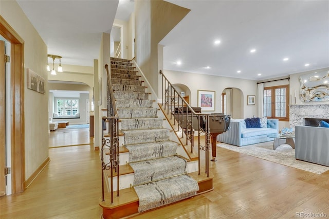 stairway with arched walkways, recessed lighting, wood finished floors, and a high end fireplace