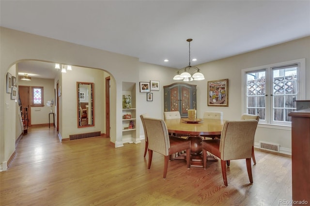 dining room with light wood-style floors, arched walkways, baseboards, and visible vents