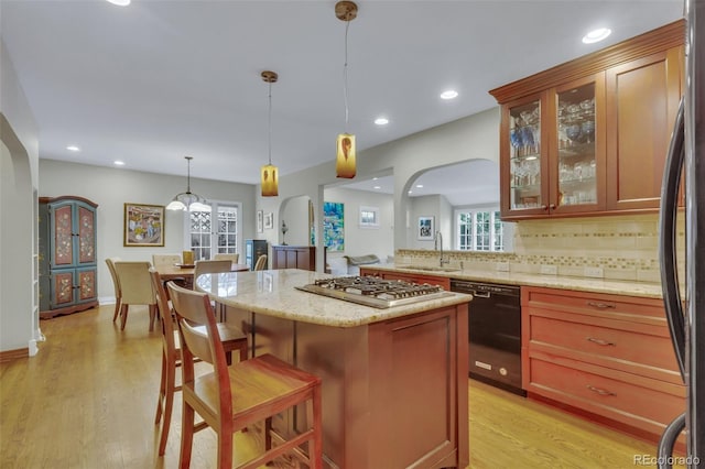kitchen with a sink, light wood-style floors, arched walkways, a kitchen breakfast bar, and black appliances