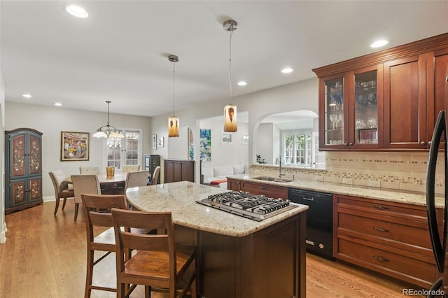 kitchen with a kitchen bar, arched walkways, stainless steel gas cooktop, a sink, and black dishwasher