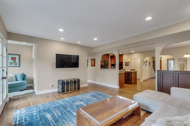 living area featuring light wood finished floors, arched walkways, recessed lighting, baseboards, and wine cooler