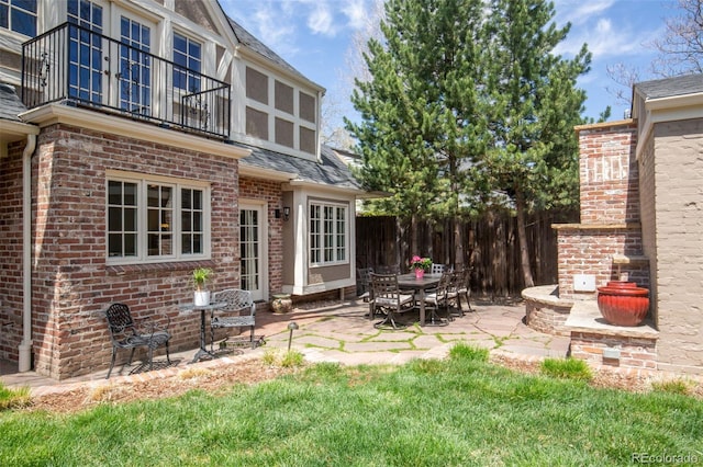 exterior space featuring brick siding, fence, a balcony, a patio, and a shingled roof