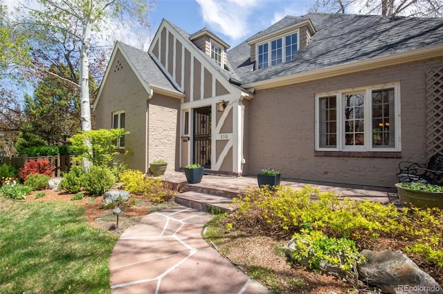 view of exterior entry featuring brick siding, fence, and roof with shingles