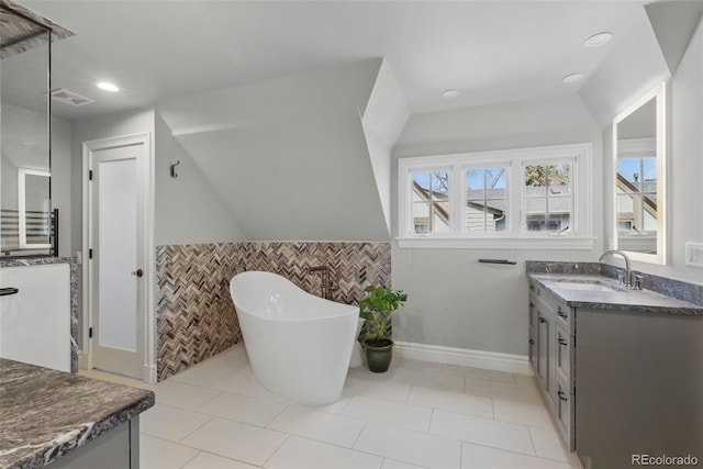 bathroom with wainscoting, vanity, tile patterned floors, tile walls, and a soaking tub