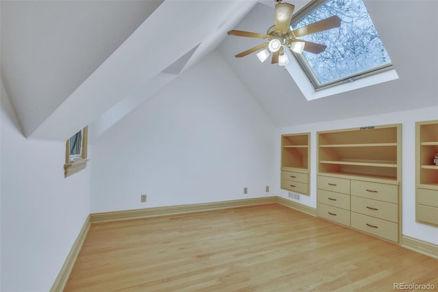 bonus room with a ceiling fan, built in shelves, lofted ceiling with skylight, and light wood-type flooring