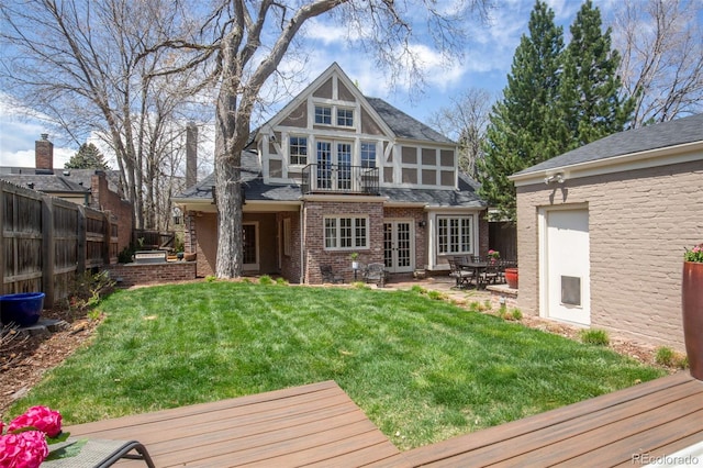 rear view of house with french doors, a deck, brick siding, fence, and a yard