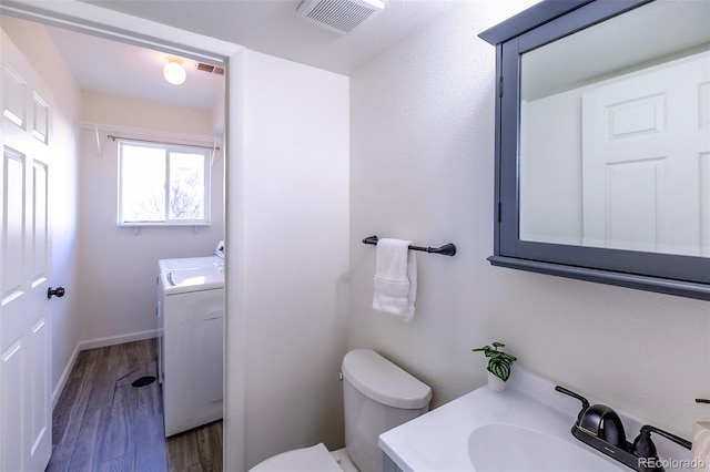 bathroom featuring wood-type flooring, vanity, toilet, and washer / dryer