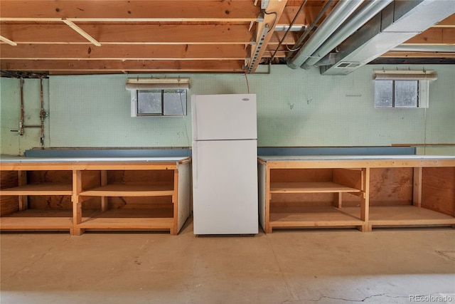 basement featuring a wealth of natural light, a workshop area, and white fridge