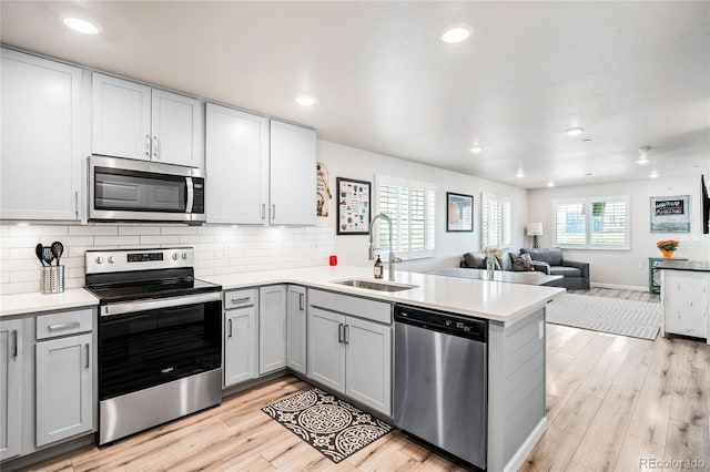 kitchen with kitchen peninsula, sink, stainless steel appliances, and light wood-type flooring