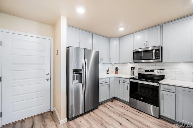 kitchen with gray cabinets, light hardwood / wood-style floors, appliances with stainless steel finishes, and tasteful backsplash