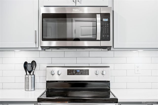 kitchen with white cabinets, backsplash, light stone countertops, and stainless steel appliances