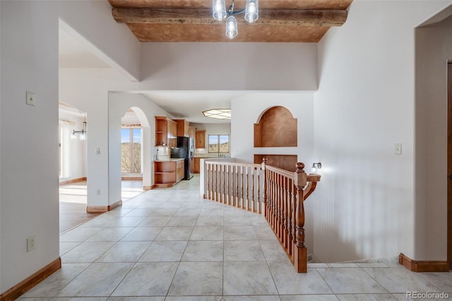 hallway with baseboards, arched walkways, a high ceiling, and beam ceiling