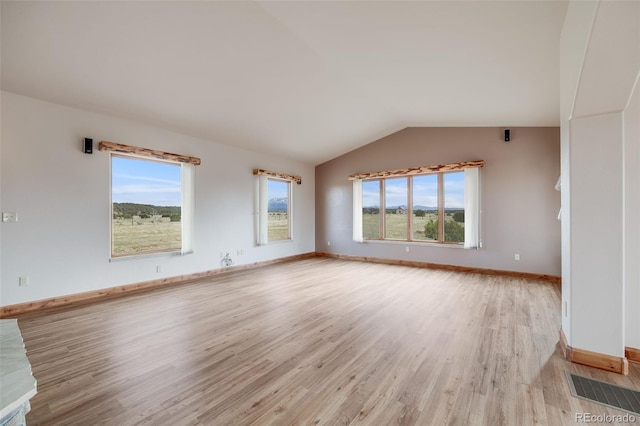 unfurnished room featuring visible vents, light wood finished floors, vaulted ceiling, and a wealth of natural light