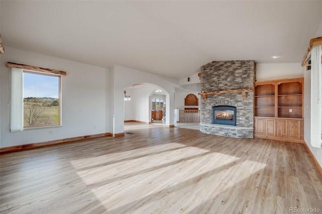 unfurnished living room featuring arched walkways, a fireplace, baseboards, lofted ceiling, and light wood-style flooring