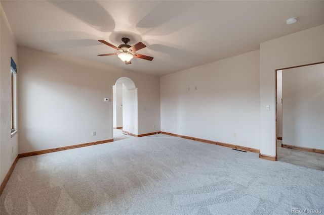 empty room with arched walkways, baseboards, light carpet, and a ceiling fan