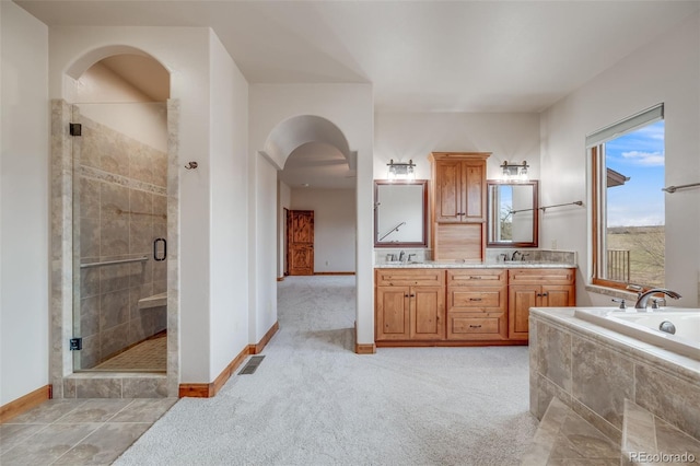 bathroom featuring double vanity, a bath, visible vents, a stall shower, and baseboards