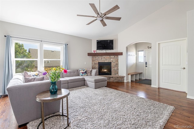 living room with ceiling fan, dark hardwood / wood-style floors, a stone fireplace, and lofted ceiling