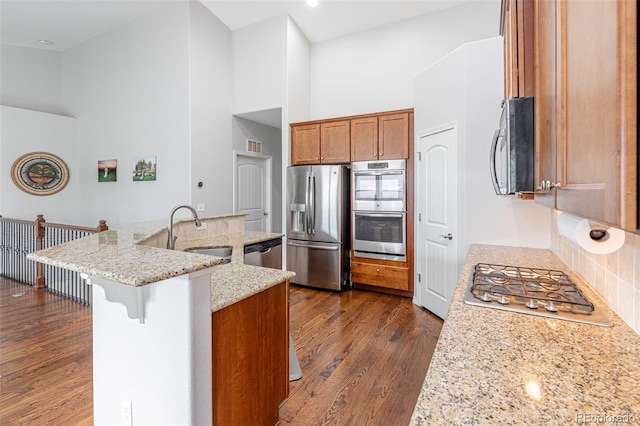 kitchen with stainless steel appliances, light stone counters, sink, and a high ceiling