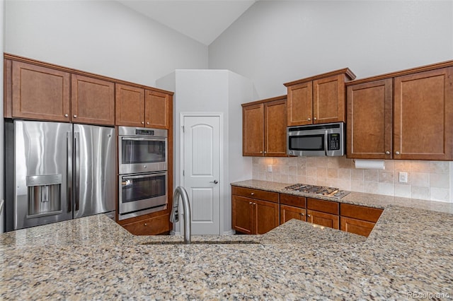 kitchen featuring high vaulted ceiling, light stone counters, appliances with stainless steel finishes, and tasteful backsplash