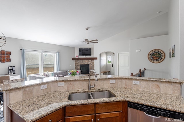 kitchen featuring a stone fireplace, lofted ceiling, sink, stainless steel dishwasher, and light stone countertops