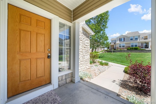 view of exterior entry featuring stone siding, a lawn, and a residential view