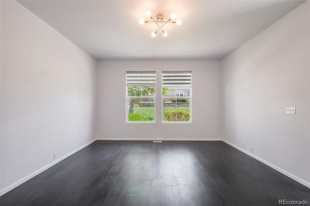 spare room featuring a chandelier, baseboards, and dark wood finished floors