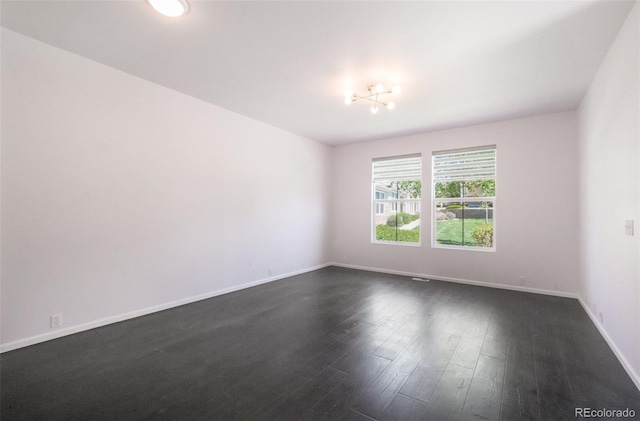 spare room with dark wood finished floors, baseboards, and a chandelier
