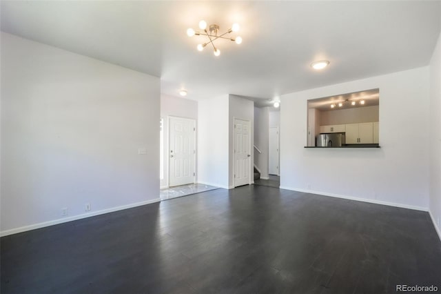 unfurnished living room with dark wood-style flooring, a chandelier, baseboards, and stairway