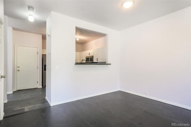 spare room featuring dark wood-style floors and baseboards