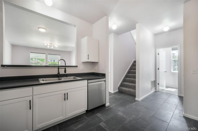 kitchen featuring stainless steel dishwasher, a sink, dark countertops, white cabinetry, and baseboards