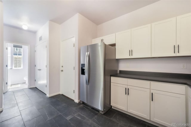 kitchen featuring stainless steel fridge, dark countertops, white cabinetry, and baseboards