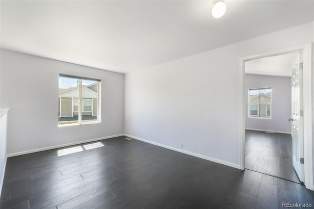 spare room featuring dark wood-style floors, plenty of natural light, and baseboards