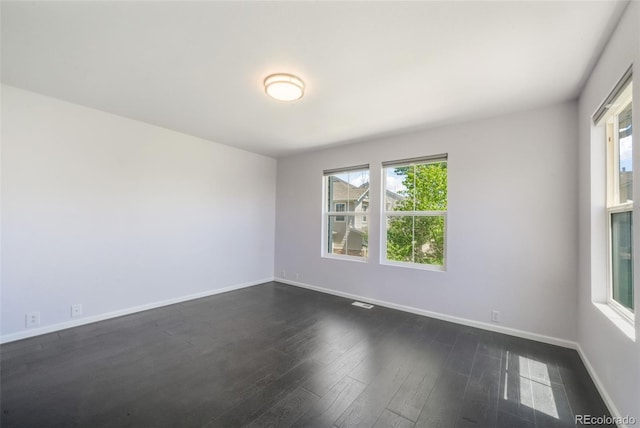 spare room featuring plenty of natural light, dark wood-style floors, and baseboards