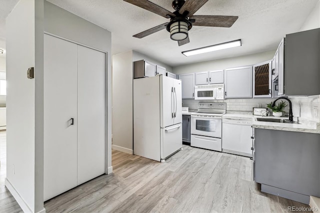 kitchen with white appliances, tasteful backsplash, light wood finished floors, light countertops, and a sink