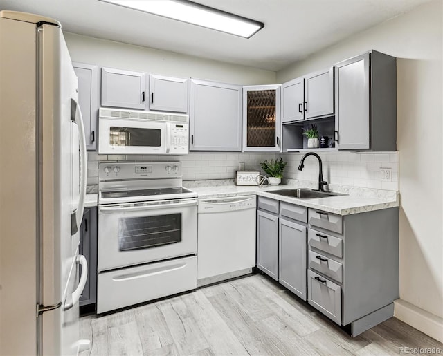 kitchen featuring light wood-type flooring, white appliances, sink, backsplash, and gray cabinetry