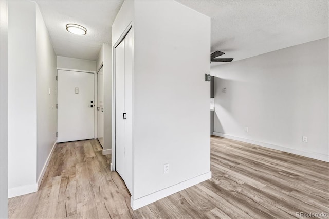 hall featuring a textured ceiling, light wood-type flooring, and baseboards